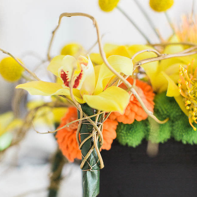 yellow orchid twisted in decorative thin roots in bouquet with orange and green blurred out flowers
