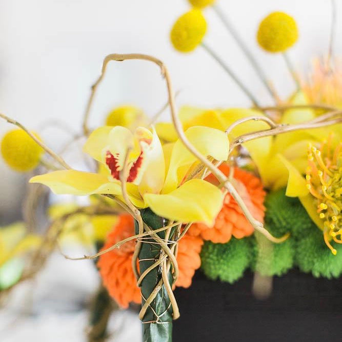 beautiful yellow orchid and other assorted pom pom flowers that are orange and green in vase