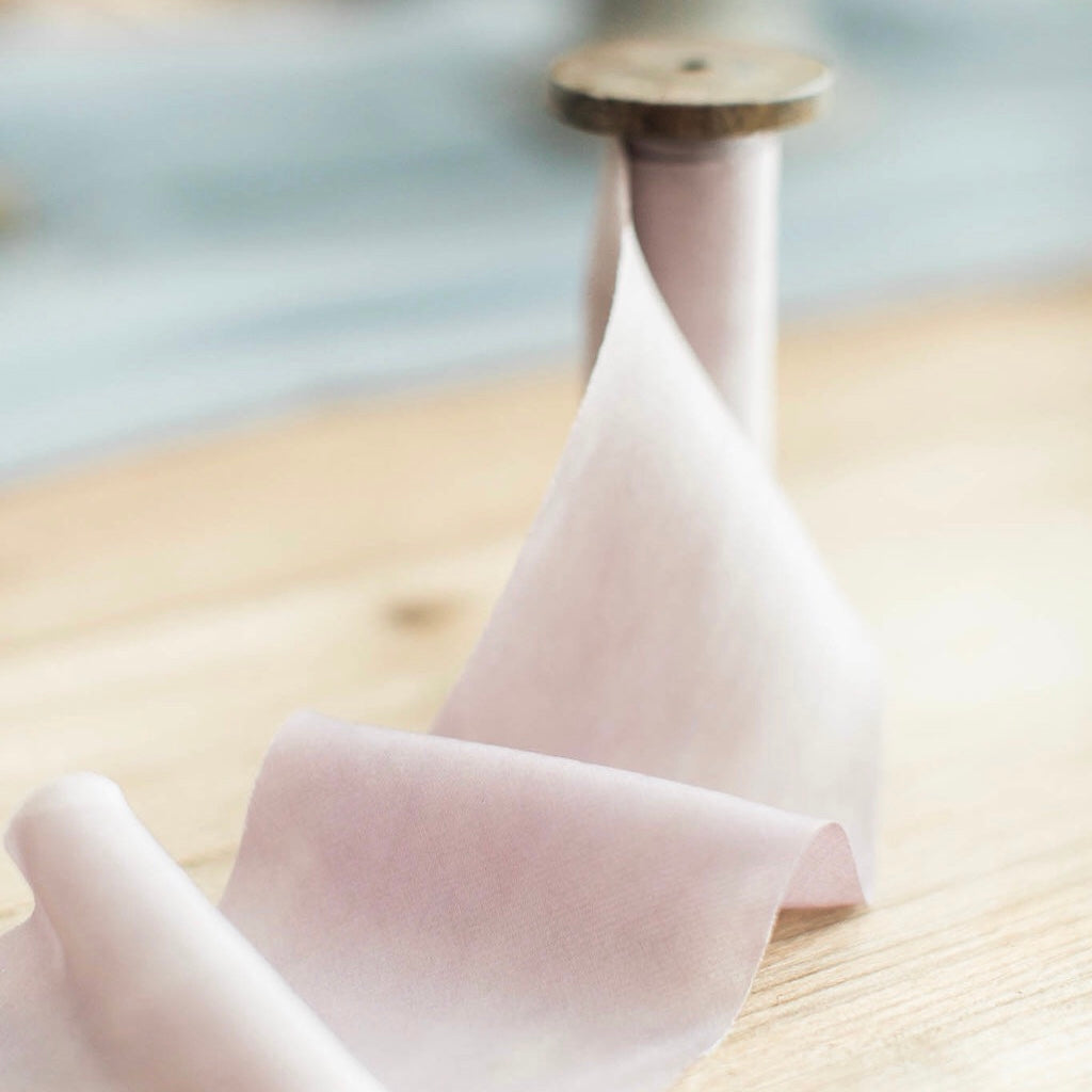 Old school medium sized wooden spool spilling out it's last beige colored cloth about 2.5 inches wide on a wooden table