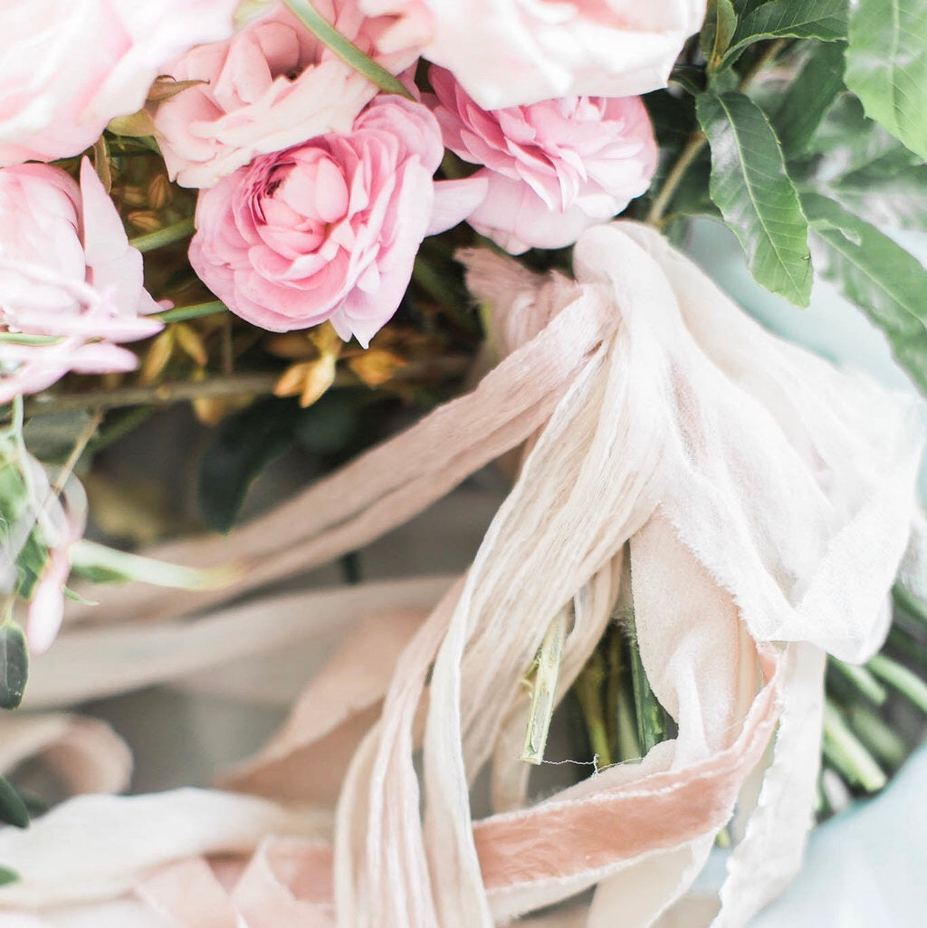 bouquet of long stemmed light pink peonies wrapped in light pink flowy ribbon