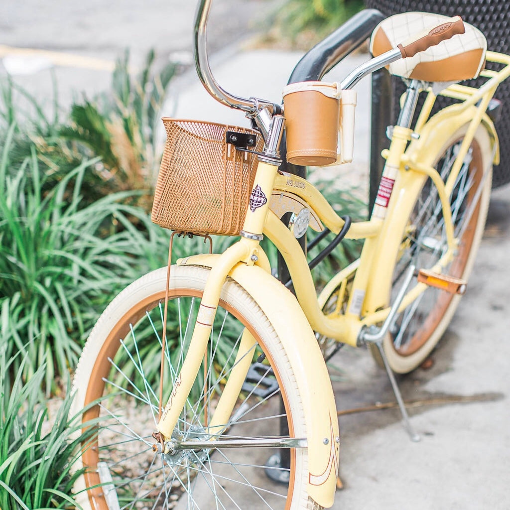 Yellow lindsey larue bicycle parked on the sidewalk beside ferns planted in ground