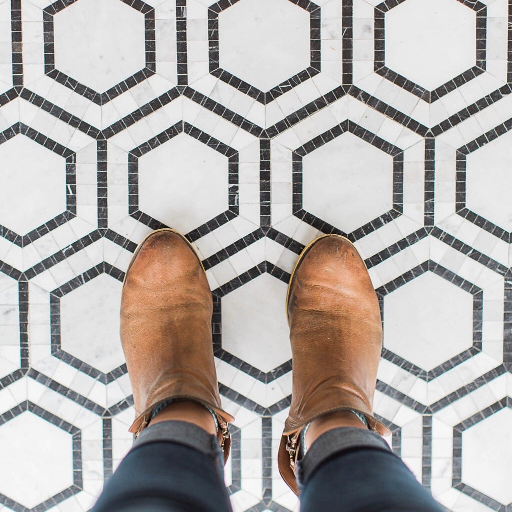 image of woman's thighs and down in tight blue jean pants with bottoms folded up wearing brown ankle boots standing on black and white hexagon shaped tiled floor