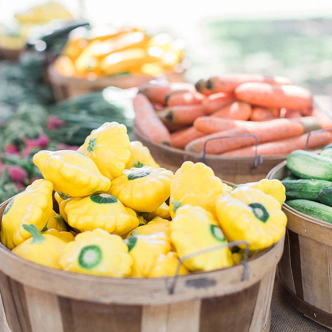 Looks like a image from the market, there are wooden baskets filled with veggies including carrots, cucumber and yellow saucer squash