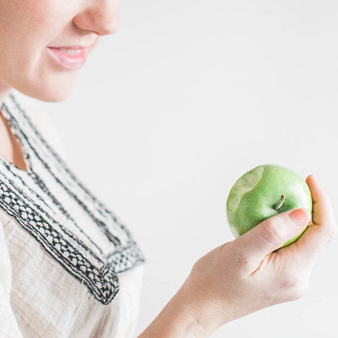 Image only shows the woman's face from the top of the nose and down, she is eating a green apple getting ready to  take another bite