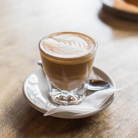 tiny cup of decorated cappuccino on saucer with napkin and spoon 