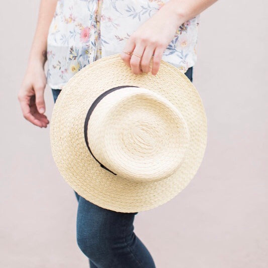 bottom half of woman in jeans and floral top holding a woven hat at her side