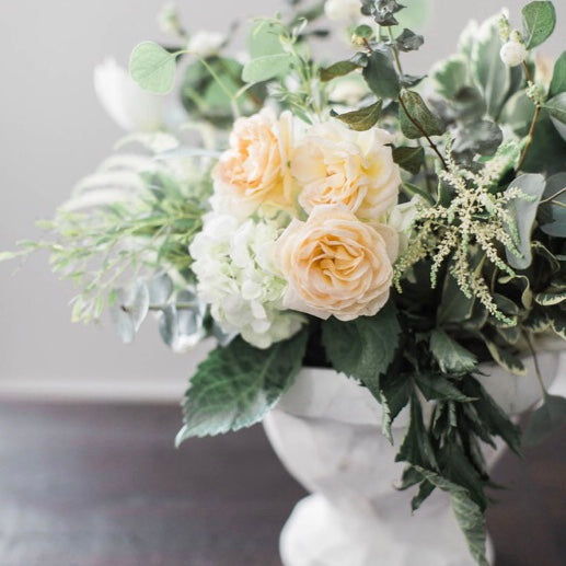 White vase with white and peach colored flowers and tons of greenery