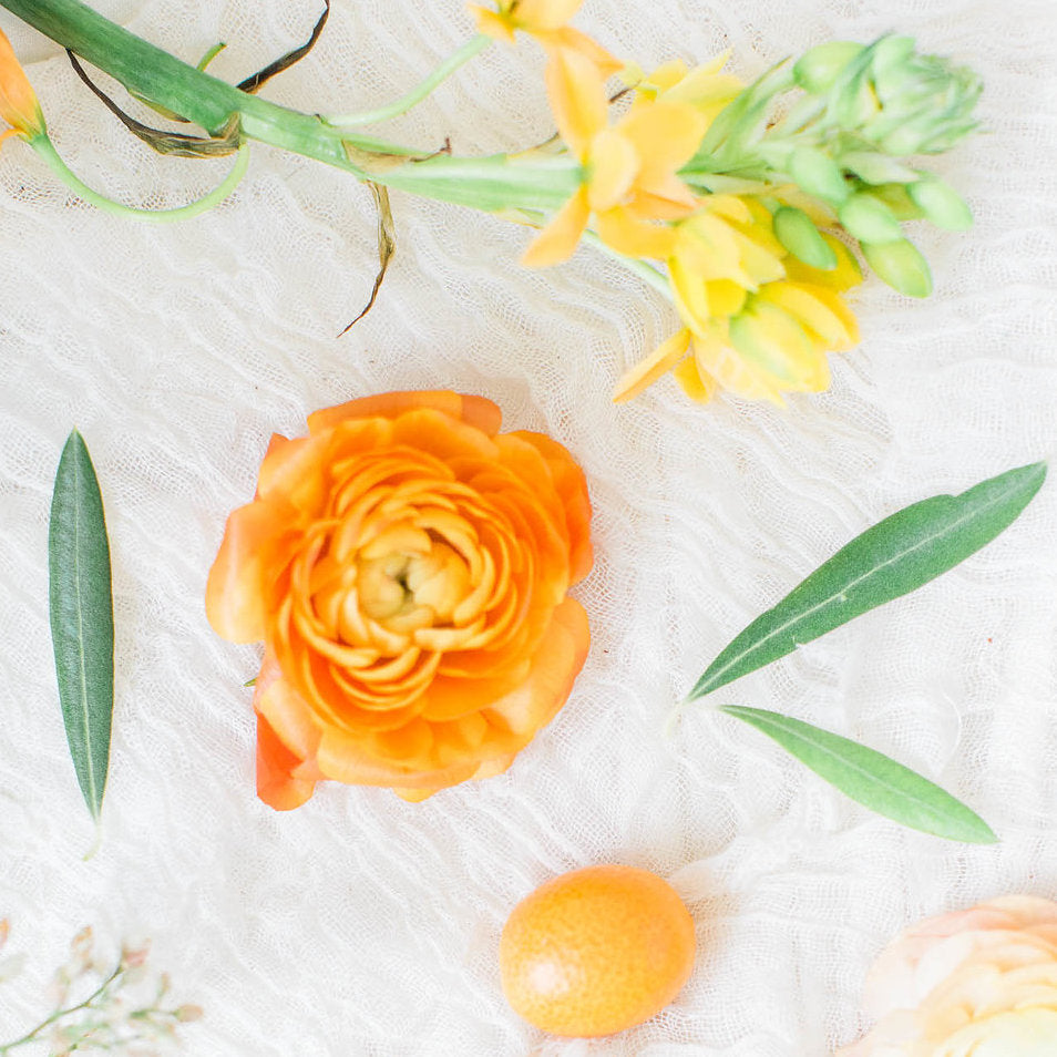 orange peony without stem arranged on table with other green and orange flowers