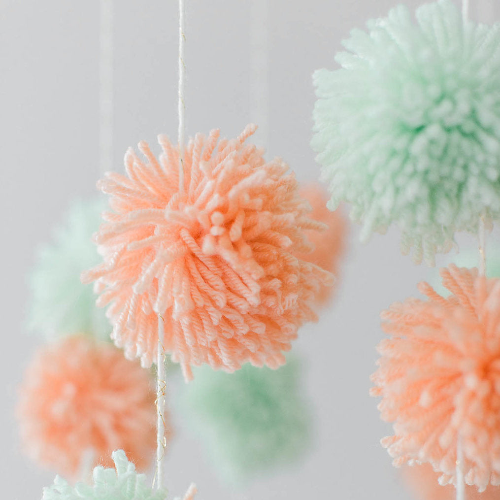 Coral and seafoam green yarn pom poms hanging on white string